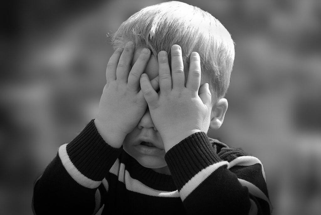 A toddler boy with his hands over his eyes.