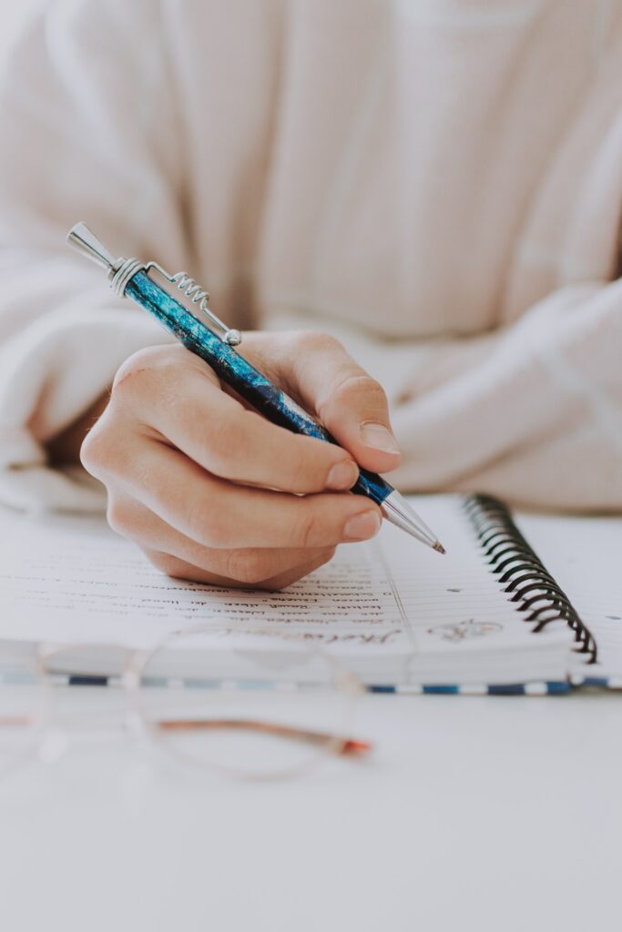 A person is writing with a pen in a notebook.